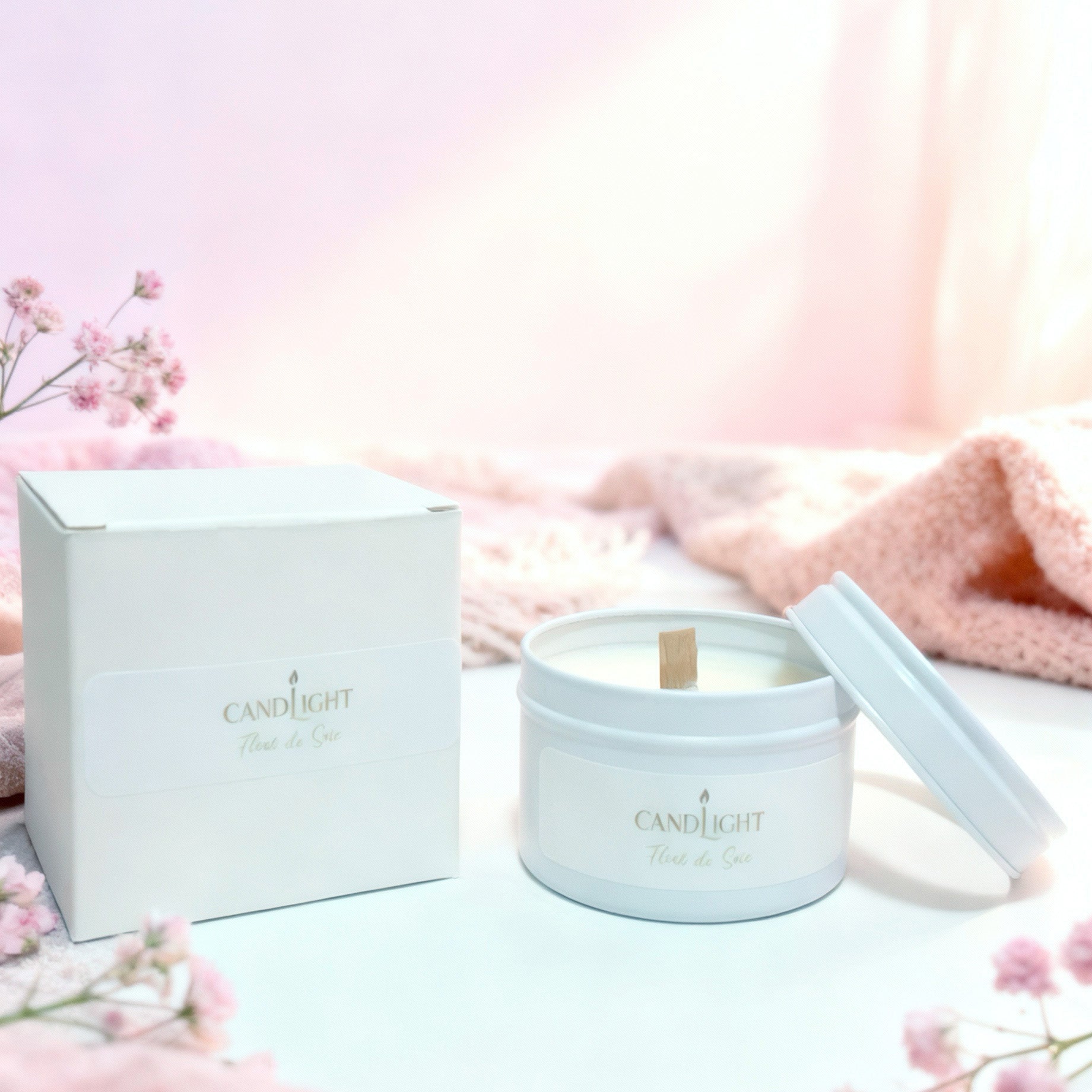 Bougie à mèche en bois dans une boite en métal blanc à côté de sa boite en carton blanc, décor blanc et pur en arrière plan